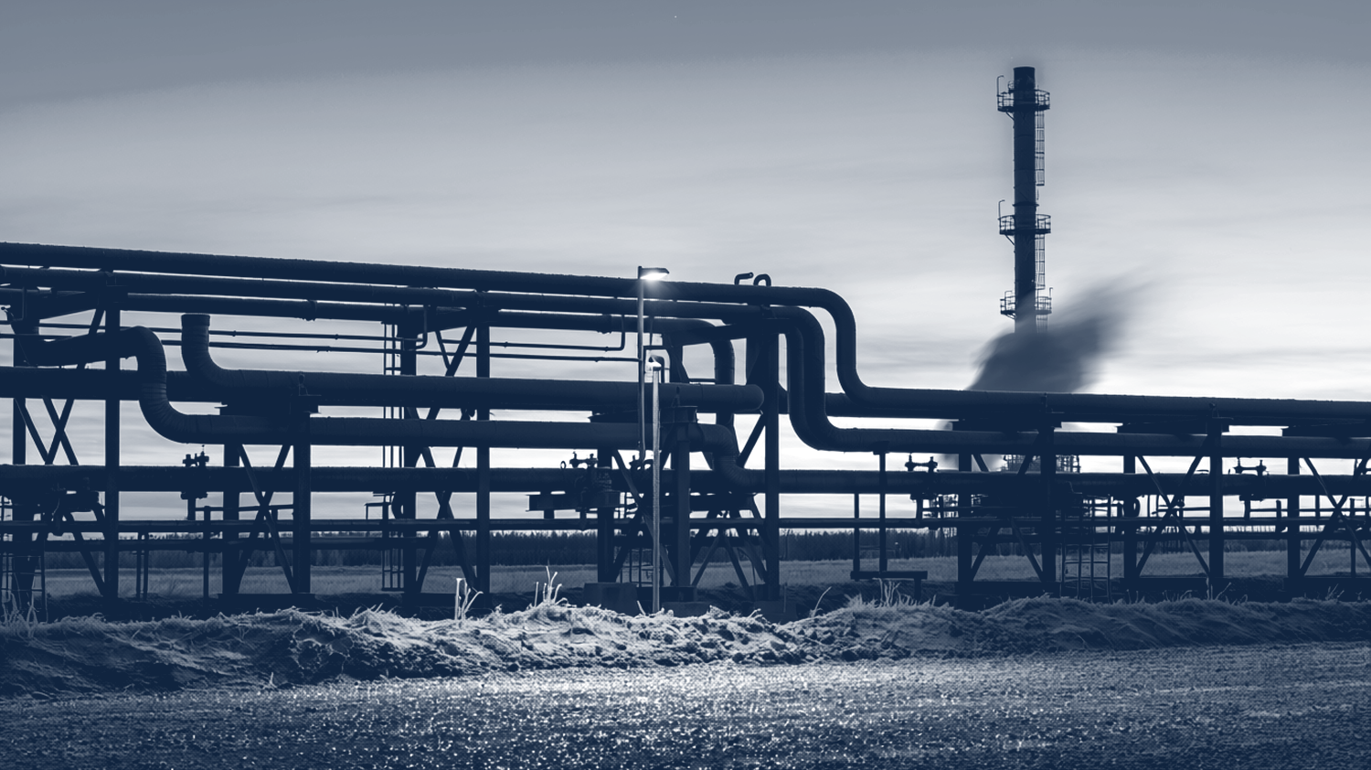 Industrial pipe rack and flare stack silhouetted against a cold dawn sky, frost on the ground.